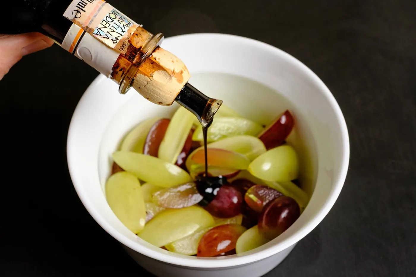 Aceto Balsamico Tradizionale fließt aus der Flasche über Trauben