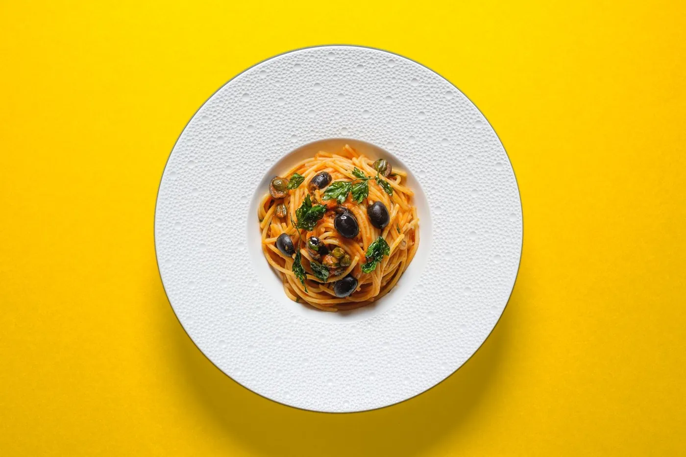 Spaghetti Puttanesca auf gelbem Grund
