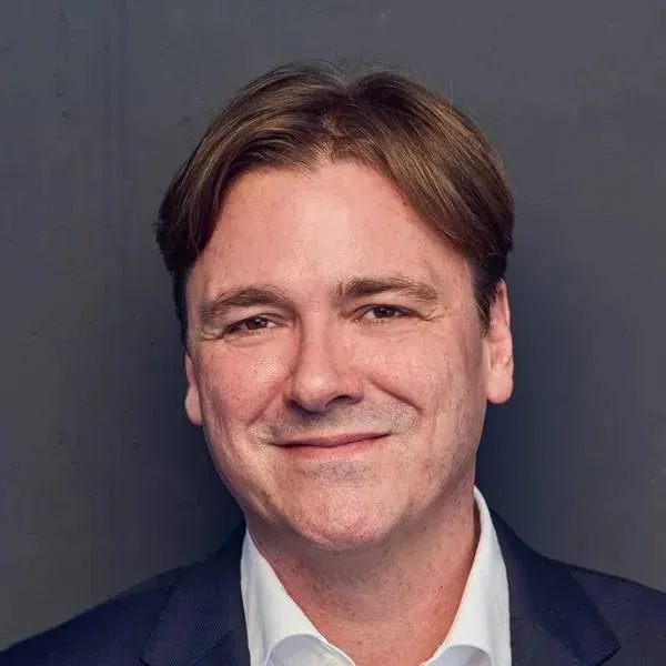 Thomas Sixt im dunklen Sakko vor grauer Wand